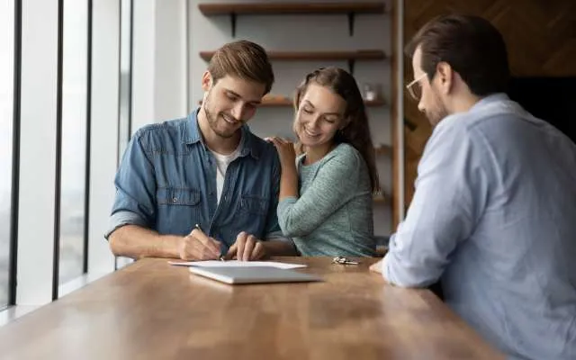 Loving young happy couple signing agreement document. Affectionate loving young happy married couple signing agreement document with professional financial advisor, lawyer or real estate agent, making deal, feeling satisfied with good service at meeting.