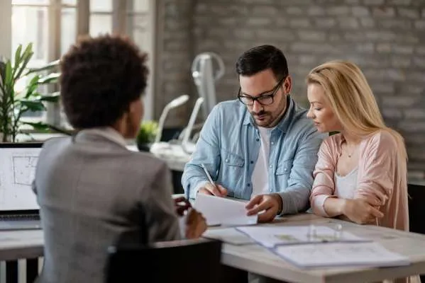 Couple signing a contract on a meeting with real estate agent. Mid adult man signing documents while being with his wife on a meeting with insurance agent.